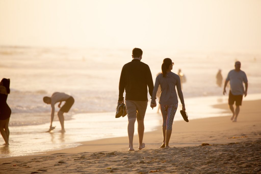 homme et femme se tenant la main en marchant sur la plage pendant la journée