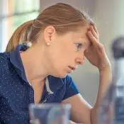 Oméga-3 et dépression : une femme anxieuse se tient le front, assise devant son travail à accomplir.