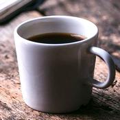 Une tasse blanche remplie de café sur une table en bois. Le café est irritant pour la vessie hyperactive.
