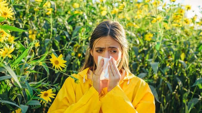 Antihistaminiques naturels : une jeune femme en veste jaune est allergique aux fleurs qui se situent tout autour d'elle