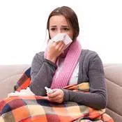 Une femme malade souffre d'un faible système immunitaire. Elle se mouche dans son canapé sous une couette colorée.
