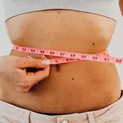 Tableau IG : l'index glycémique aide à perdre du poids. On aperçoit un ventre d'une femme mince qui mesure son tour de taille avec un ruban rose