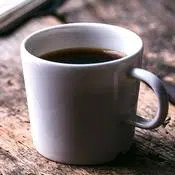 Une tasse blanche remplie de café sur une table en bois. Le café est un bon stimulant en plus d'être une boisson minceur naturelle.