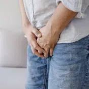 Un homme habillé en jeans et chemise semble souffrir de problèmes urinaires.