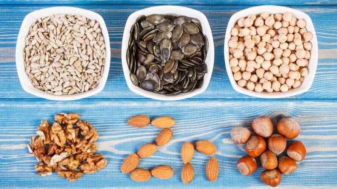 Aliments riches en zinc : il y a des noix, des amandes, des noisettes, des graines de tournesol et de courge et des pois-chiches sur une table en bois bleue